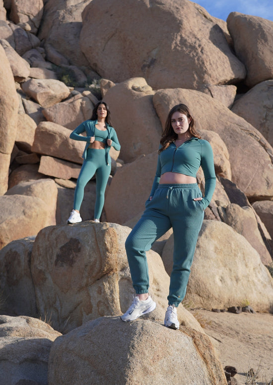Photograph features 2 models standing on big rocks wearing Crimson tavernorlando Sedona Collection outfits of pieces in the Mineral color-way.